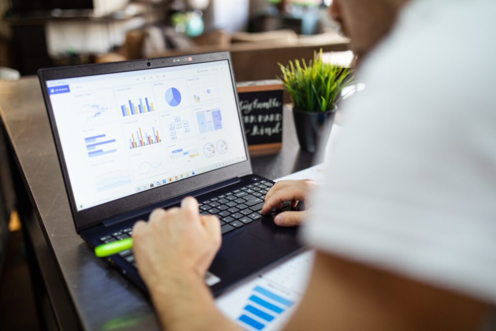 Em uma mesa branca, um laptop preto cuja tela exibe gráficos e dados, remetendo-os a métricas de marketing digital.