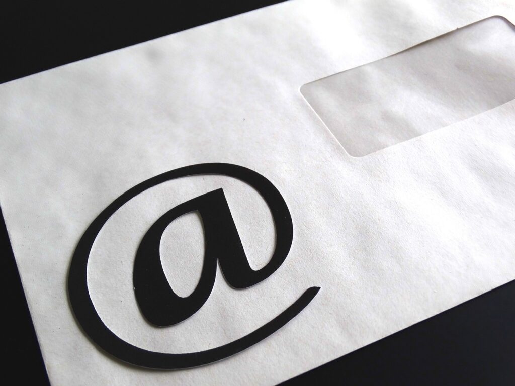 Sobre superfície preta, um envelope na cor branca está posicionado ao lado do símbolo de 