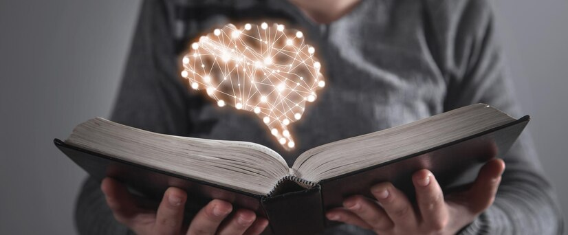 Um livro aberto no meio e segurado por duas mãos, em cima dele um cérebro com ponto luminosos.